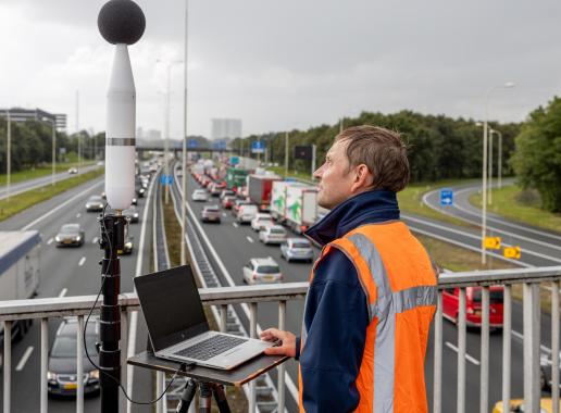 Man staat op een brug boven een snelweg met meetapparatuur voor geluid