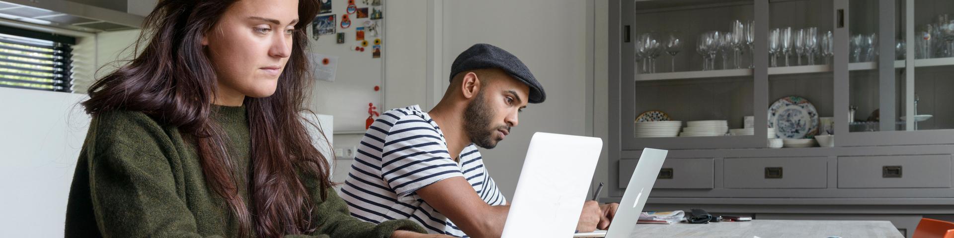 Nederland, Friesland, Leeuwarden, 30 augustus 2014, Jonge mensen werken thuis aan laptop aan grote tafel in woonkeuken, vrouw en man met notebook, computer, beeldscherm, kast met serviesgoed op de achtergrond. Foto: Tineke Dijkstra