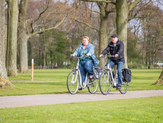 Twee personen fietsen op elektrische fietsen door het Zuiderpark in Den Haag