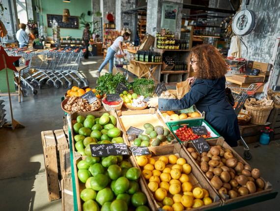 Dame met krullend haar is tussen de schappen met groenten, groenten aan het uizoeken in een winkel.