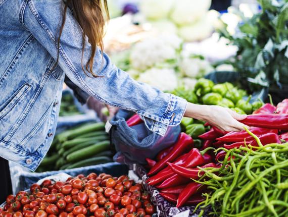 Vrouw pakt puntpaprika van een marktstal en lacht daarbij