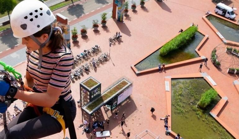 Vrouw met helm klimt een gebouw af (gezekerd) boven het vernieuwde, vergroende Lübeckplein