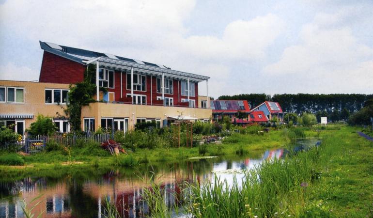 Duurzaam ecologisch wonen in Culemborg, rode huizen aan het water met veel groen afgebeeld.