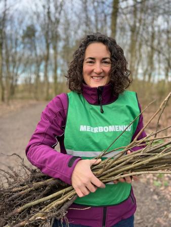 Dame lacht naar de camera en heeft boompjes in de hand om te planten