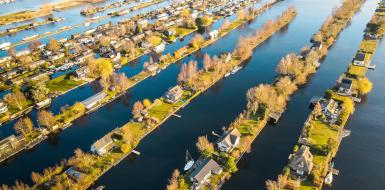 Dronebeeld van de Vinkeveense plassen van boven genomen. Je ziet huizen en veel groen en water